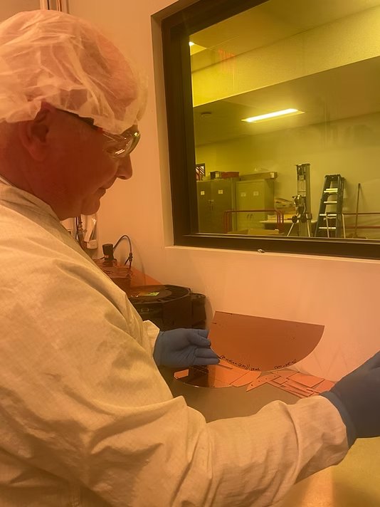 Engineer in cleanroom gear handling a semiconductor wafer during testing
